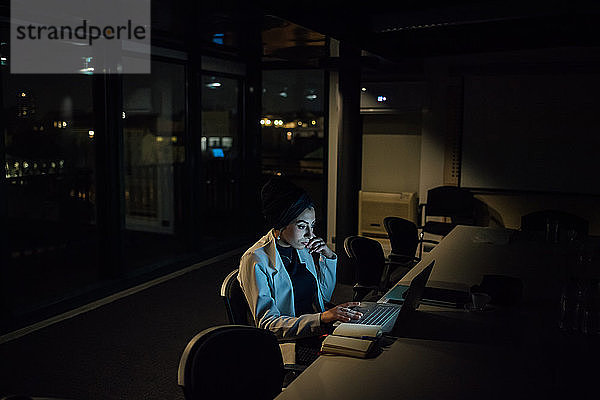 Junge Geschäftsfrau  die nachts im Büro am Laptop tippt