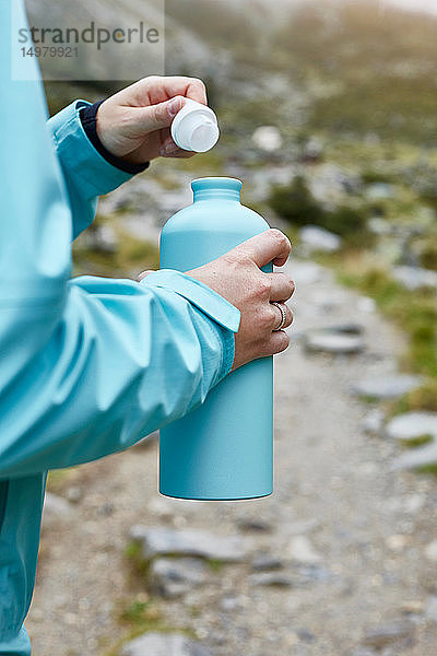 Wanderin öffnet Trinkflasche auf Feldweg  abgeschnitten