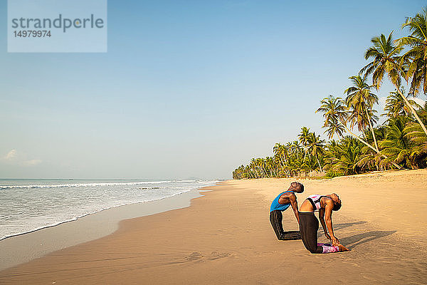 Paar praktiziert Yoga am Strand