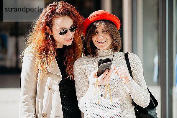 Weibliche Käuferinnen mit Smartphone vor dem Geschäft