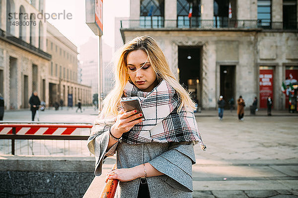 Junge Frau betrachtet Smartphone auf der Straße in der Stadt