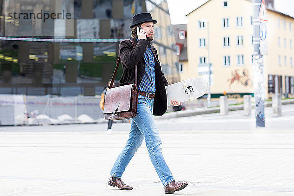 Männlicher Skateboarder schlendert auf dem Stadtplatz und telefoniert mit seinem Smartphone  Freiburg  Baden-Württemberg  Deutschland