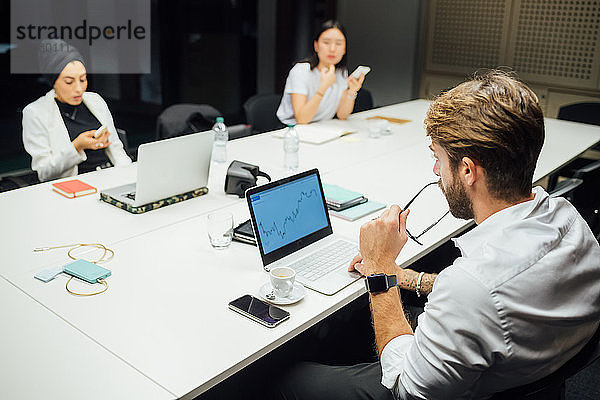 Geschäftsfrau betrachtet Laptop und Smartphones am Konferenztisch