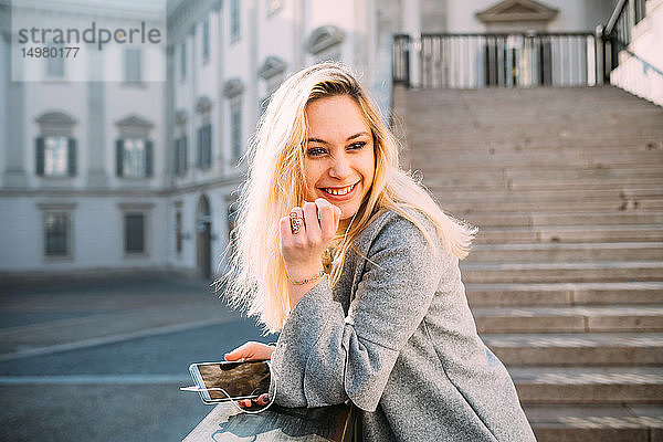 Junge Frau mit langen blonden Haaren  die auf einer Treppe Smartphone-Musik hört  Mailand  Italien