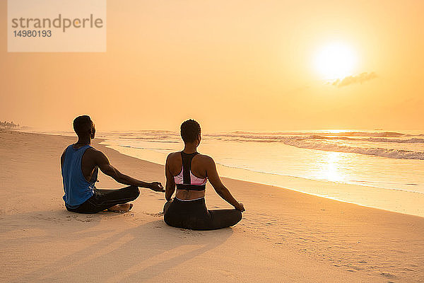 Paar praktiziert Yoga am Strand