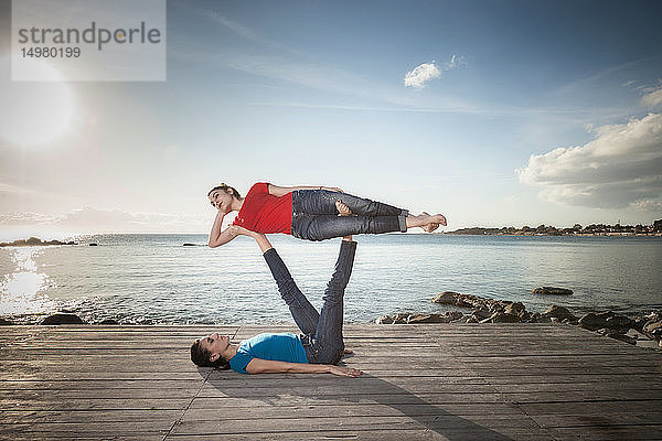 Frauen praktizieren Akro-Yoga am Meer