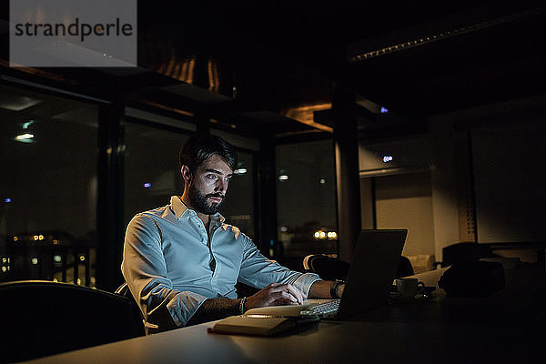 Mittelgroßer erwachsener Geschäftsmann nachts im Büro beim Tippen am Laptop