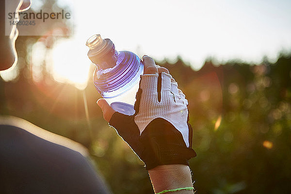 Radfahrerin mit Wasserflasche in der Hand  über die Schulter geschnitten