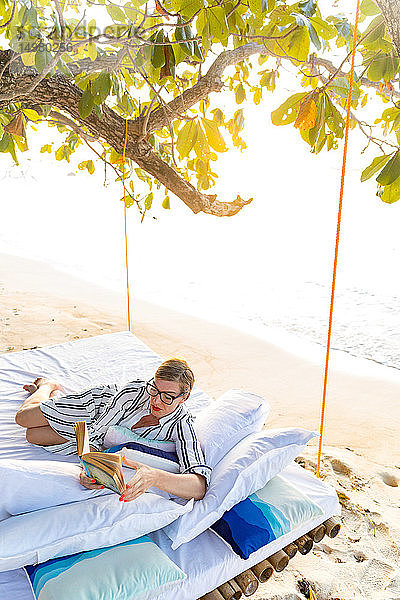 Frau liest Buch auf Schaukelbett am Strand  Insel Ginto  Linapacan  Philippinen