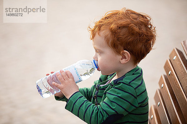 Junge trinkt Wasser auf Parkbank