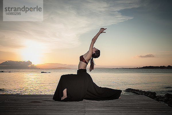 Frau praktiziert Yoga am Meer