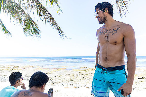 Freunde sprechen und benutzen Smartphone am Strand  Pagudpud  Ilocos Norte  Philippinen