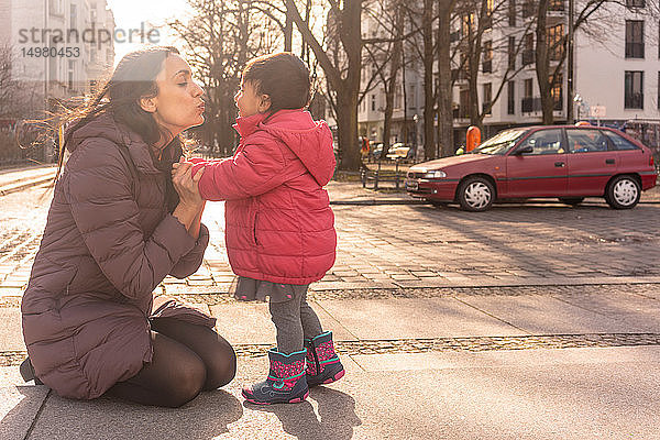 Mutter küsst Tochter auf Bürgersteig