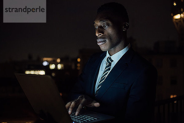 Junger Geschäftsmann tippt nachts auf dem Bürobalkon am Laptop  Nahaufnahme