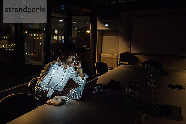 Müde junger Geschäftsmann nachts im Büro beim Tippen am Laptop