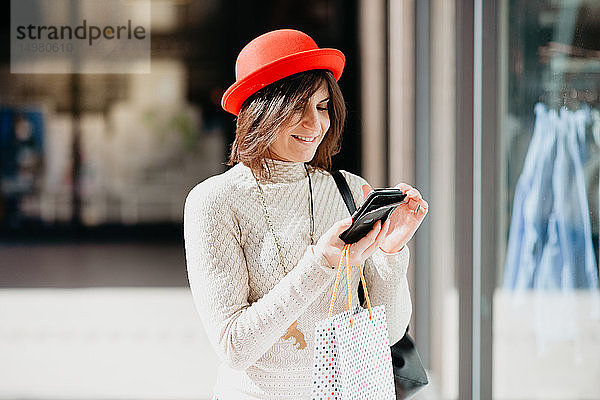 Weibliche Käuferin mit Smartphone vor dem Geschäft