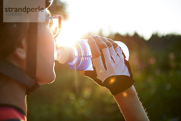 Radfahrerin  die aus einer Wasserflasche trinkt  über die Schulter gestürzt