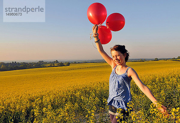 Mädchen mit roten Luftballons auf Rapsfeld  Eastbourne  East Sussex  Vereinigtes Königreich