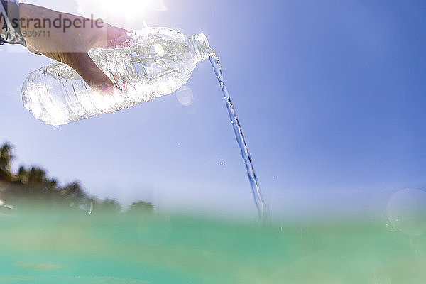 Frau schüttet abgefülltes Wasser ins Meer