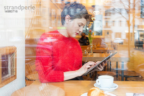 Mittlere erwachsene Frau im Café mit digitalem Tablet-Touchscreen  Fensteransicht