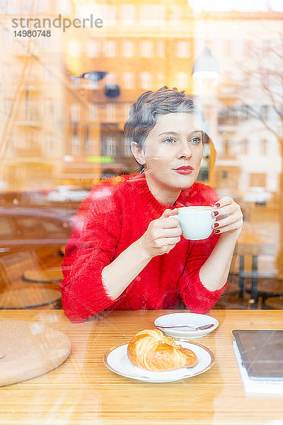 Mittelgroße erwachsene Frau im Café  die Kaffee trinkt und aus dem Fenster schaut