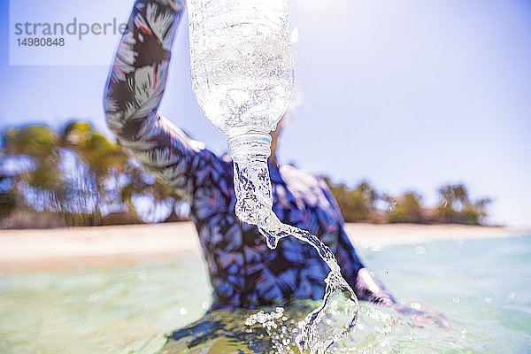 Frau schüttet abgefülltes Wasser ins Meer