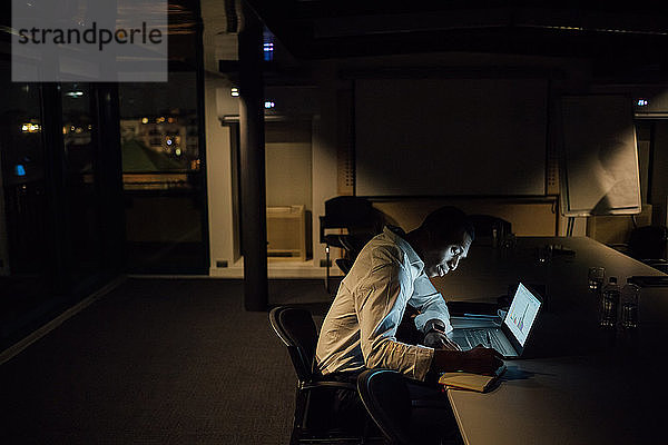 Junger Geschäftsmann nachts im Büro und macht sich Notizen vom Laptop