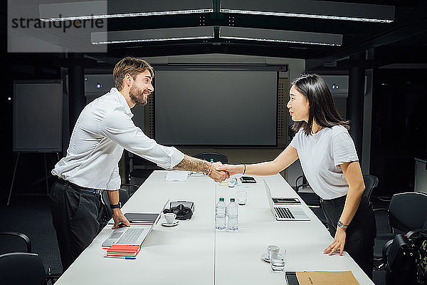 Geschäftsfrau und Mann schütteln sich die Hand am Konferenztisch