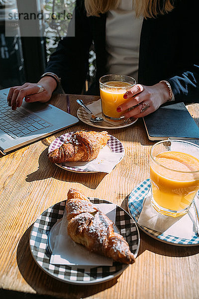 Junge Frau am Cafe-Tisch auf dem Bürgersteig beim Tippen am Laptop  beschnitten