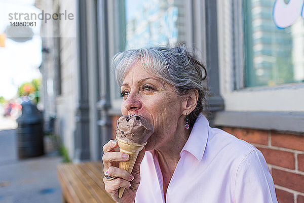 Ältere Frau sitzt auf dem Bürgersteig und isst Schokoeiswaffel