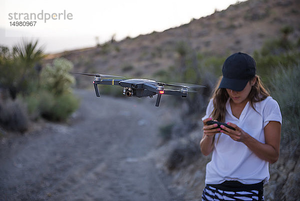 Frau bedient Drohne (unbemanntes Luftfahrzeug) auf ländlichem Feldweg