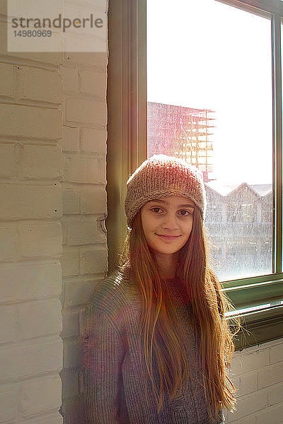 Teenagermädchen mit langen braunen Haaren und Strickmütze am Fenster  Porträt