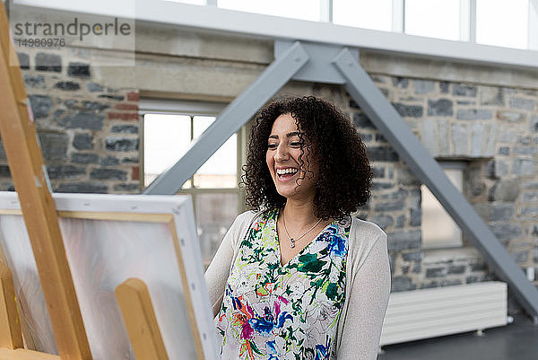 Junge Malerin lacht  während sie im Atelier Leinwand malt