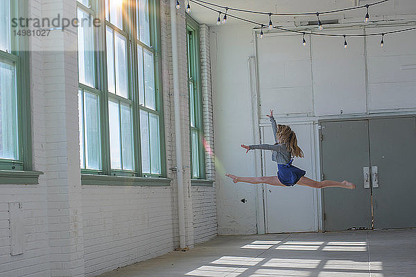 Teenager-Mädchen mit langen braunen Haaren springt im Tanzstudio in die Luft