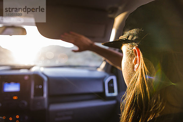 Frau als Beifahrerin auf dem Vordersitz eines Autos  die die Augen vor Sonnenlicht schützt  Blick über die Schulter