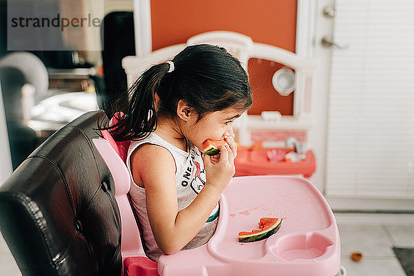 Mädchen im Hochstuhl beim Essen von Wassermelone  Seitenansicht
