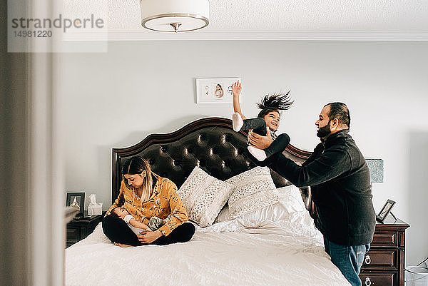 Mädchen wird vom Vater auf das Bett geworfen  neben der Mutter  die den kleinen Bruder stillt