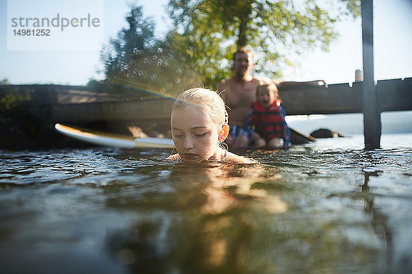Mädchen schwimmt und spielt im See  Vater und Schwester im Hintergrund