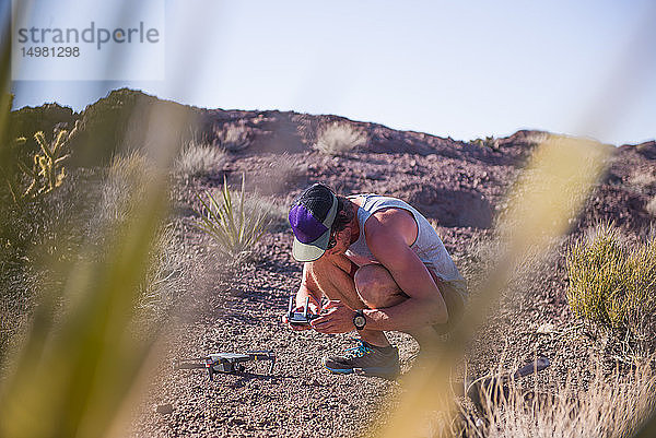 Mann hockt in der Wüste und schaut auf Steuerpult für Drohne (unbemanntes Luftfahrzeug)