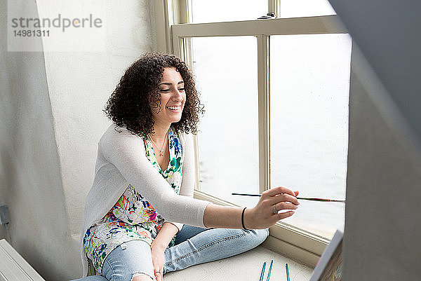 Junge Malerin malt Leinwand auf Atelier-Fensterbrett