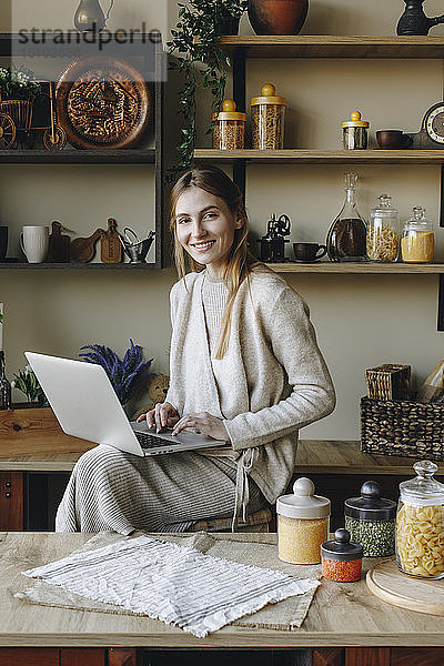 Lächelnde junge Frau mit Laptop in der Küche