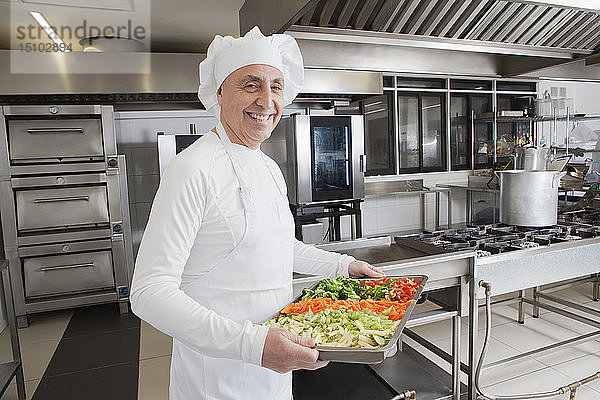 Lächelnder Koch mit einem Tablett voller Gemüse