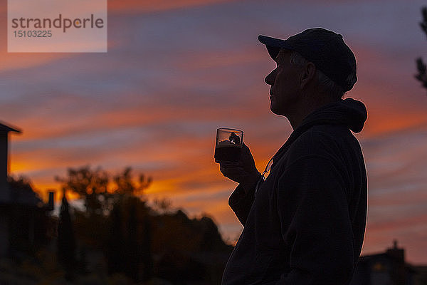 Silhouette eines Mannes mit Kaffeetasse bei Sonnenuntergang