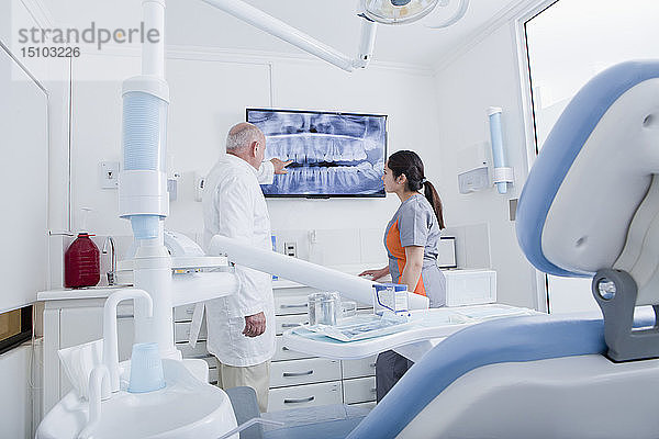 Zahnarzt und Zahnhygienikerin untersuchen Röntgenaufnahmen auf einem Fernsehbildschirm