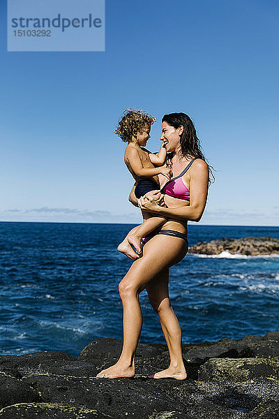 Mutter trägt ihren Sohn auf Felsen am Meer