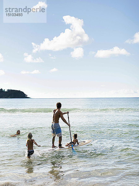 Mann auf Paddleboard mit seinen Kindern am Strand