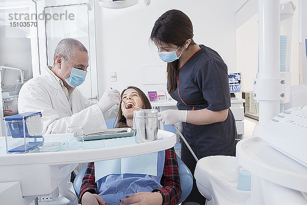 Zahnarzt und Zahnhygienikerin reinigen die Zähne eines Patienten