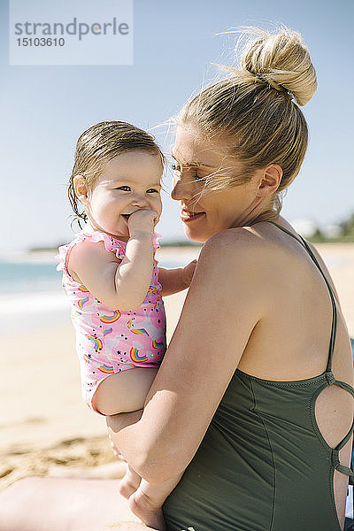 Mutter trägt ihr kleines Mädchen am Strand