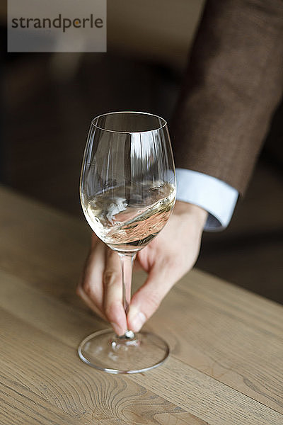 Die Hände eines Mannes  der ein Glas Weißwein schwenkt