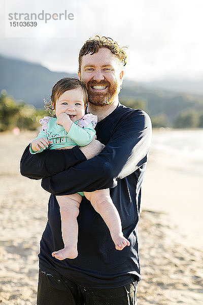 Mann hält seine kleine Tochter am Strand